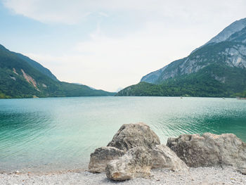 Stones on shore of blue green water. village and lake molveno at the foot of the brenta dolomites