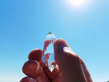 Cropped hand holding crystal against clear blue sky