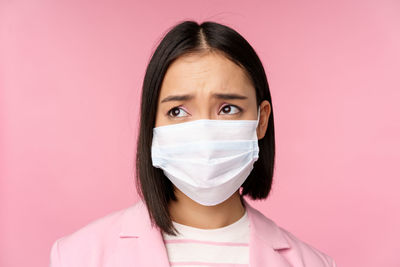 Portrait of young woman wearing mask against pink background