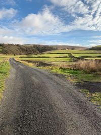 Scenic view of road amidst field against sky