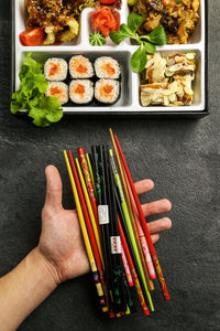 Directly above shot of cropped hand holding various chopsticks by sushi