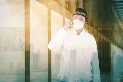 Portrait of young man looking away while standing against window