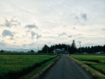 Road passing through field against cloudy sky