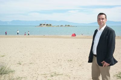 Man wearing blazer standing at beach on sunny day