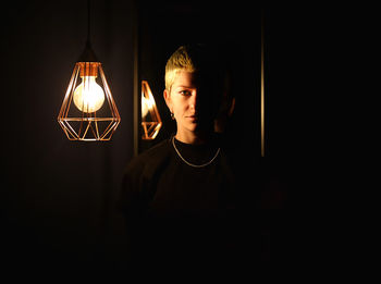 Young man looking at illuminated lamp in darkroom