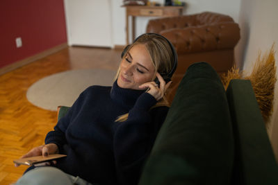 Woman listens to music with headphones lying down on her couch  mobile phone, urban living.