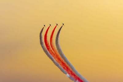 Low angle view of airshow against orange sky