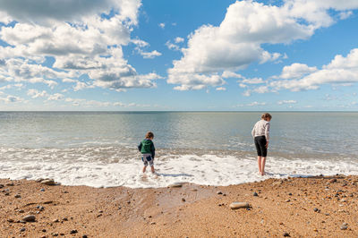 Full length of sibling standing at shore against sky