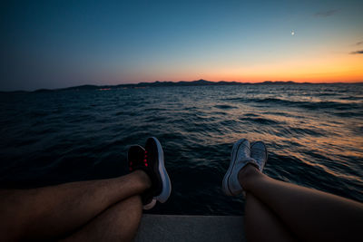 Low section of person relaxing on sea against sky during sunset