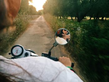 Friends reflecting on side-view mirror of motor scooter at road