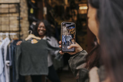 Young woman photographing female friend trying on clothes