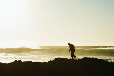 Side view of silhouette man walking on rock formation by sea