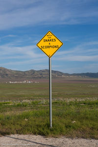 Information sign on road by field against sky