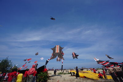 Low angle view of people looking at kites flying against blue sky