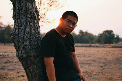 Man standing by tree trunk on field