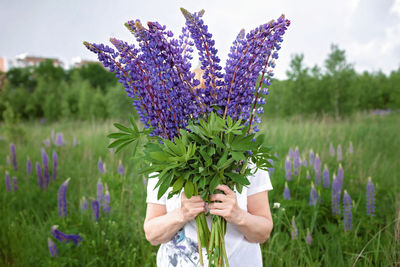 Elderly woman get a beautiful bouquet of purple lupines in blooming field, active in retirement