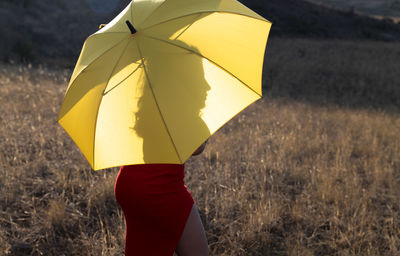 Woman in red dress holding yellow umbrella while standing on field in summer