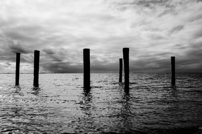 Wooden posts in sea against sky