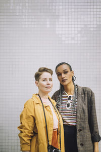 Portrait of confident young woman standing with girlfriend in front of wall