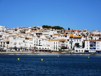 Sailboats in sea by townscape against clear blue sky