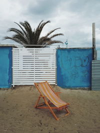 Empty chairs and palm tree on beach against sky