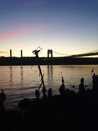 Silhouette bridge over river against sky during sunset