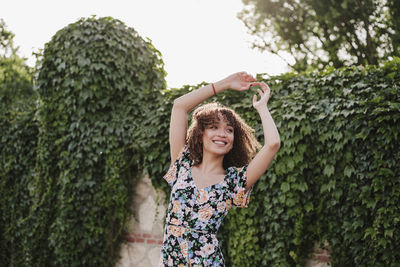 Happy woman with arms raised against trees