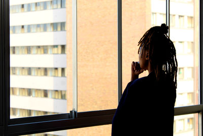 Woman with hand on chin standing against window