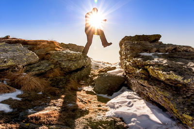 Silhouette man jumping on rocks during sunny day