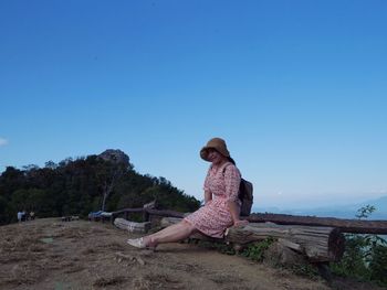 Woman sitting on land against clear blue sky