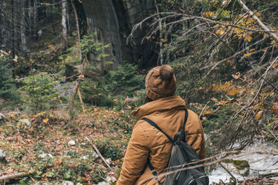 Back view of female hiker wearing yellow jacker and backpack, standing in autumn forest