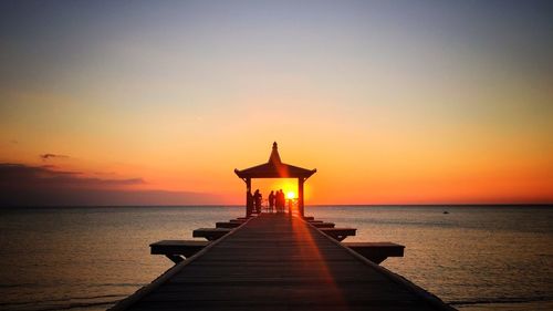 Silhouette people on gazebo by sea against sky during sunset