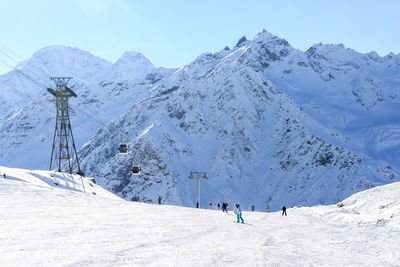 A wide ski slope against a backdrop of sharp snowy mountains and blue skies