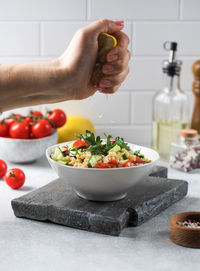 A hand squeezes the juice from a lemon into a vegetarian salad of bulgur and vegetables. 