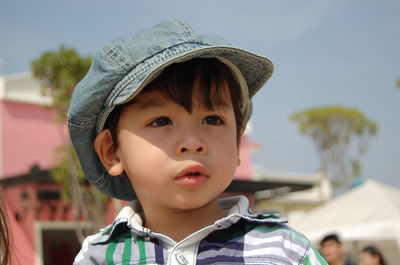 Cute boy wearing cap looking away while standing against sky