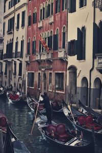 Rear view full length of man sailing gondola on canal by buildings