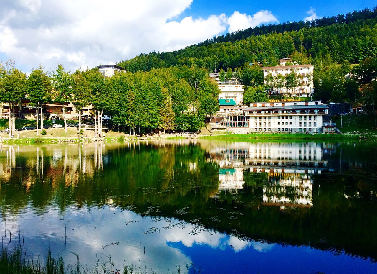 reflection, water, tree, architecture, built structure, building exterior, lake, sky, tranquility, waterfront, tranquil scene, standing water, house, scenics, nature, green color, beauty in nature, cloud, cloud - sky, pond