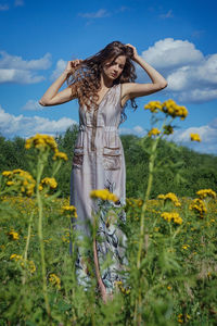 Woman with hands in hair standing on field against sky