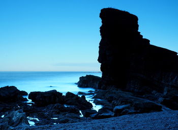 Rocks on beach against clear blue sky