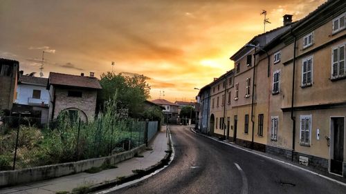 Empty road by buildings against sky during sunset