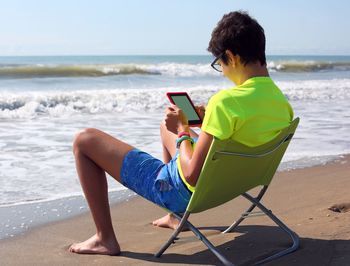 Young man using mobile phone while sitting on beach