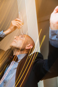 Side view of concentrated male in elegant costume putting glass with champagne on forehead while having fun at christmas party