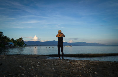 Rear view of woman standing at beach against sky