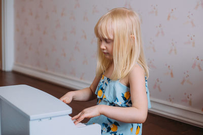 Little blonde girl plays a toy piano at home. musical development in childhood