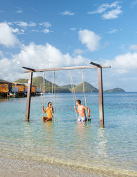 Rear view of woman swinging in sea against sky