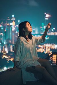 Young woman with arms raised in city against sky at night