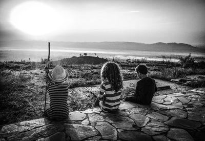 Rear view of friends sitting on wall against sky