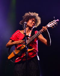 Young woman playing guitar against black background