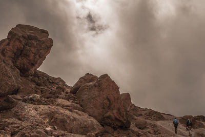 Rear view of people climbing mountain against cloudy sky