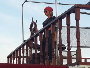 Low angle view of boy on railing against sky